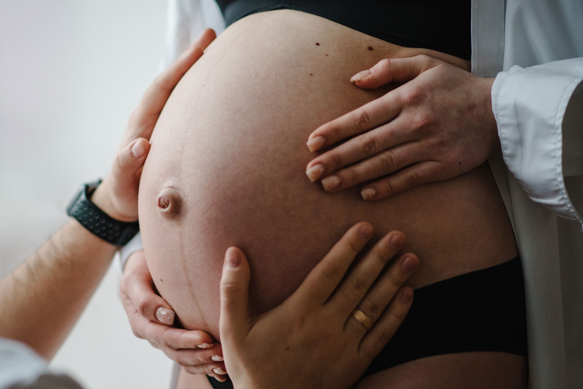 Waiting baby. Loving couple. Cropped image of beloved husband holding hand on belly of pregnant wife. Pregnant woman, loving handsome man hugging tummy at home. Parenthood concept. Nine months closeup